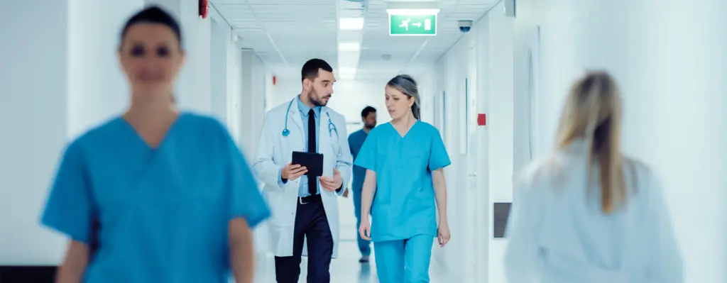 Ein Arzt und eine Krankenschwester laufen sich unterhalten über einen Krankenhausflur