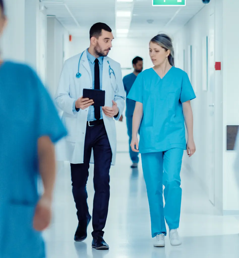 Ein Arzt und eine Krankenschwester laufen sich unterhalten über einen Krankenhausflur
