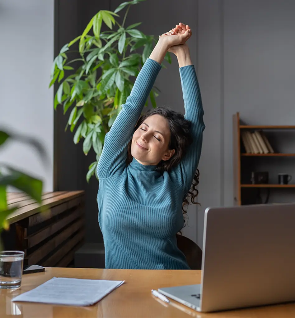 Eine Frau sitzt im Homeoffice an ihrem Laptop und streckt die Arm nach oben