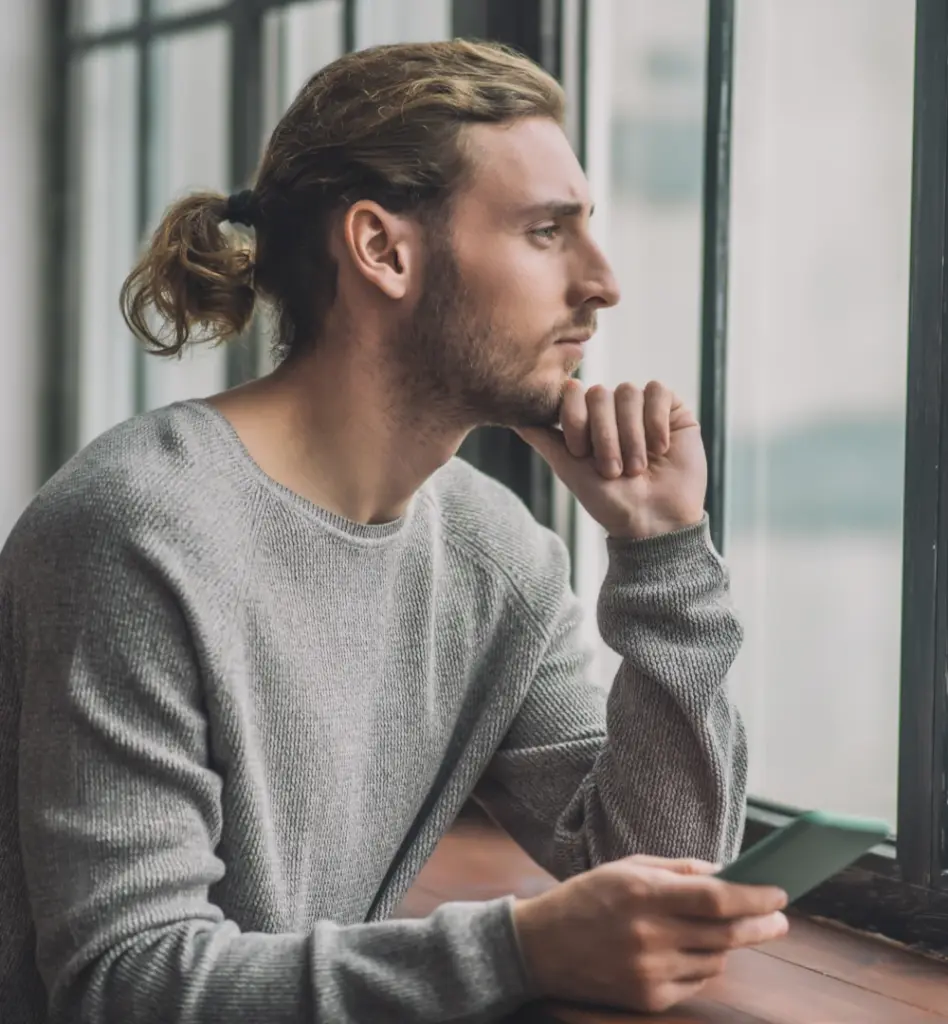 Ein junger Mann sitze nachdenklich vor dem Fenster, seinen Kopf in die Hand gestützt
