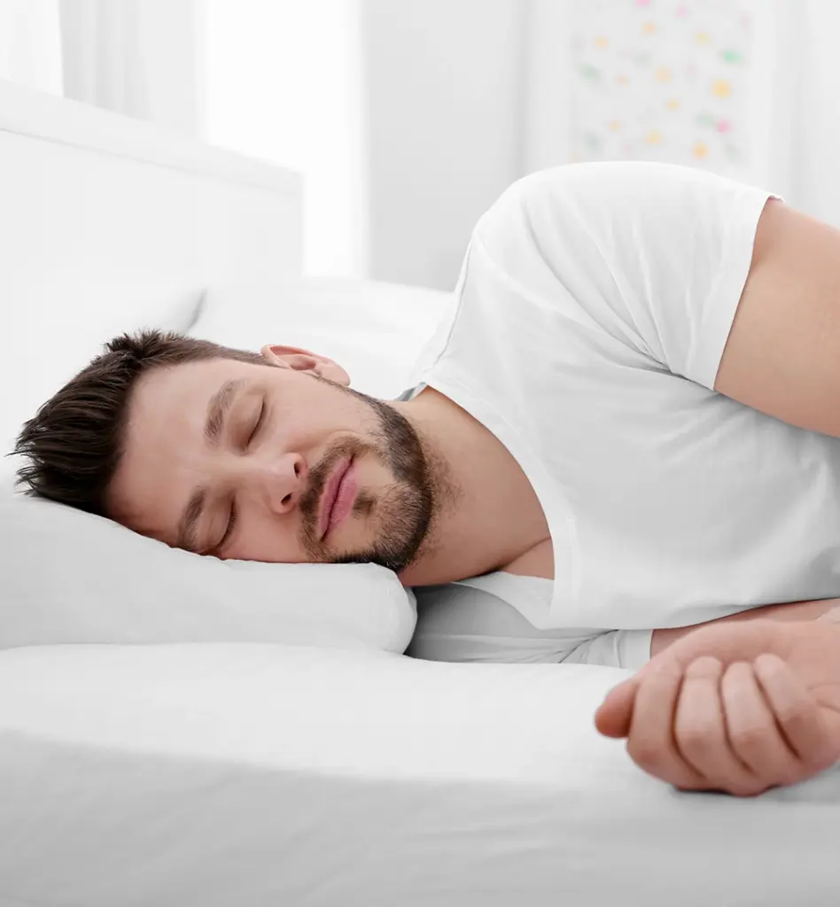Ein junger Mann liegt auf der Seit im Bett und schläft