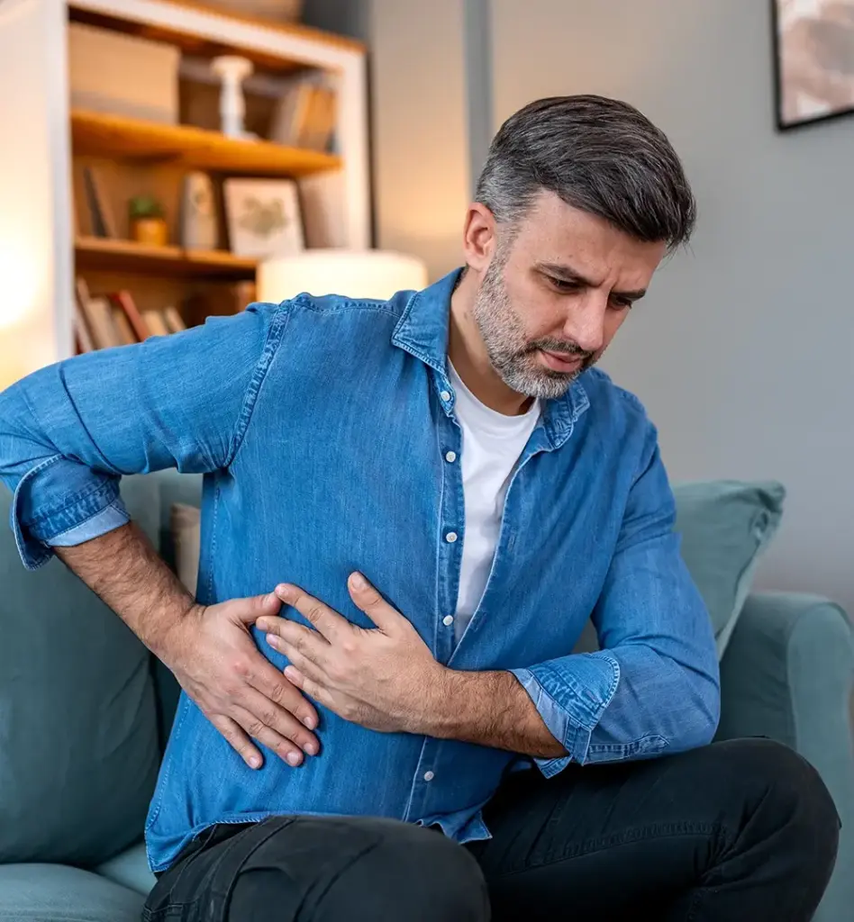 Ein Mann sitzt auf dem Sofa und greift sich vor Schmerz seitlich an die Brust