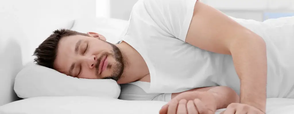 Ein junger Mann liegt auf der Seit im Bett und schläft