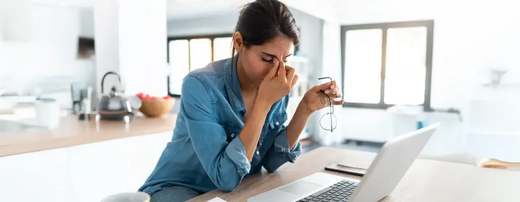 Das Bild zeigt eine Frau am Laptop. Sie ist erschöpft und fasst sich müde ins Gesicht wobei sie die Augen geschlossen hat.