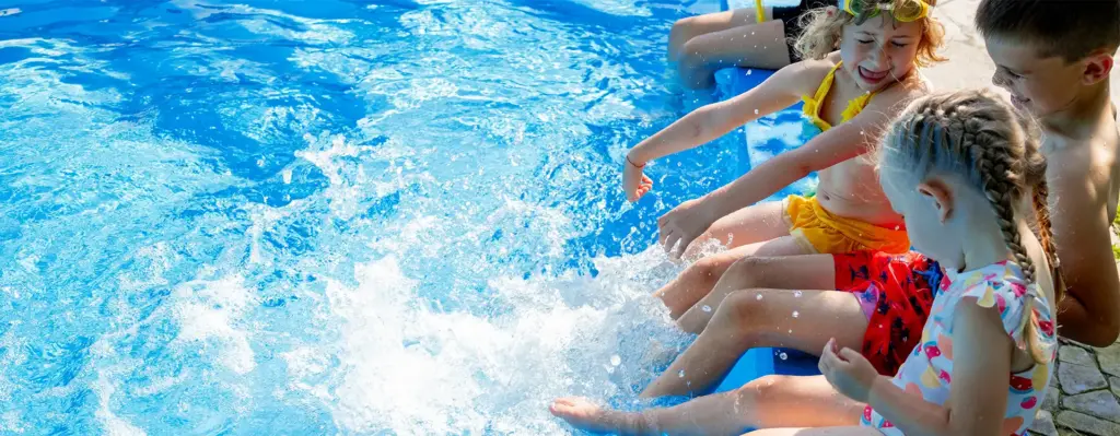 Kinder sitzen am Beckenrand eines Pools und strampeln mit den Beinen im Wasser