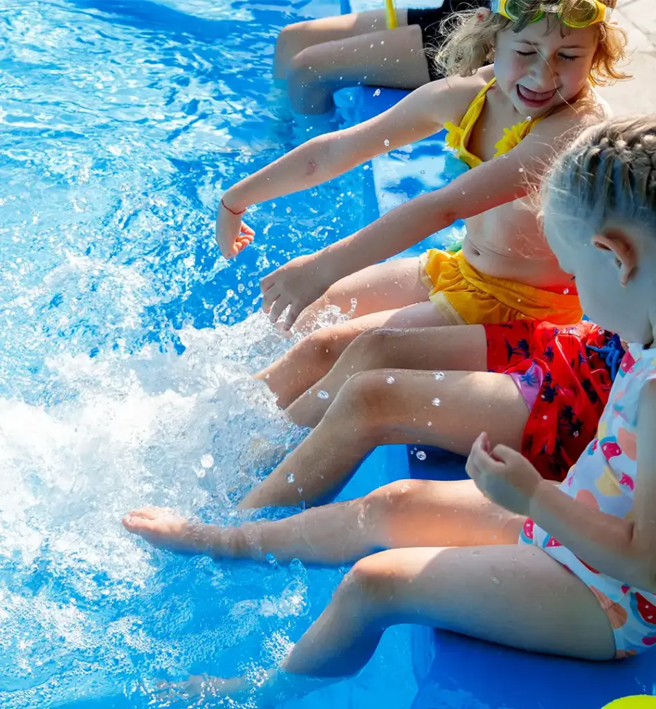 Kinder sitzen am Beckenrand eines Pools und strampeln mit den Beinen im Wasser