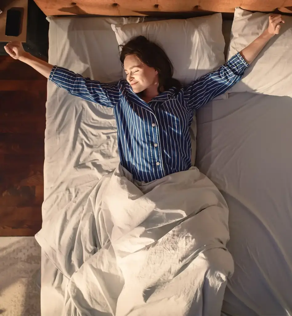 Eine Frau streckt sich beim Aufwachen m Bett in der Morgensonne