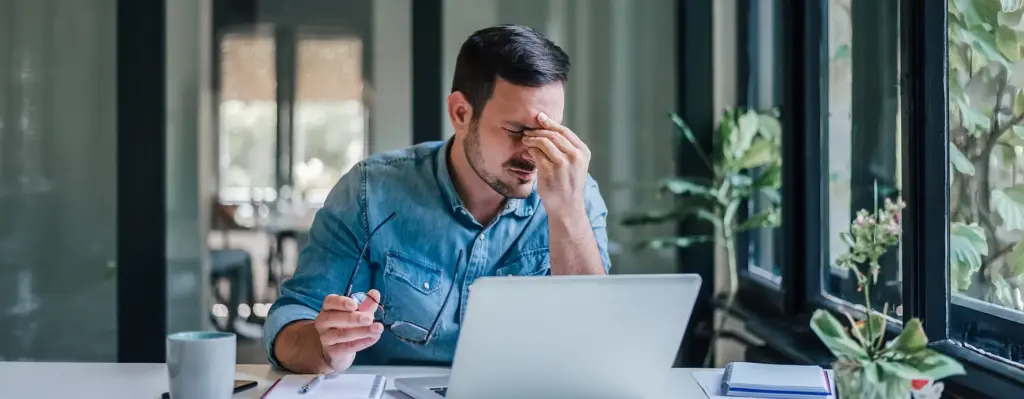 Ein Mann sitzt vor seinem Laptop und reibt sich die Augen
