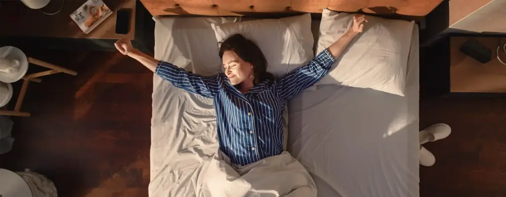 Eine Frau streckt sich beim Aufwachen m Bett in der Morgensonne